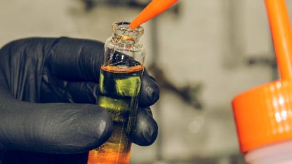 Gloved hand testing fragrance oil from a vial